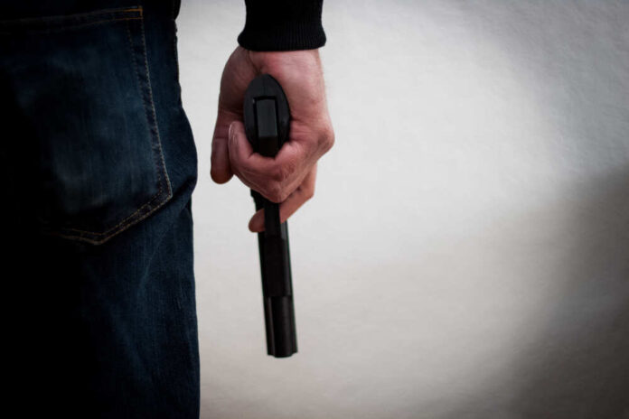 Killer,Holding,A,Gun,To,His,Feet,,White,Background,In
