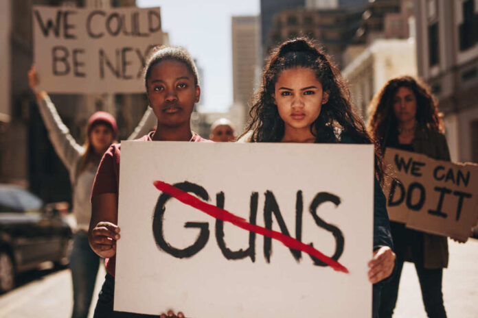 Two,Girls,Holding,A,Banner,With,Word,Guns,Strikethrough.,Women