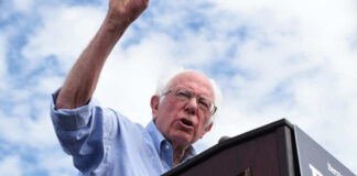 Man speaking at a podium under cloudy sky.