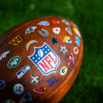 NFL football with team logos on grass field.