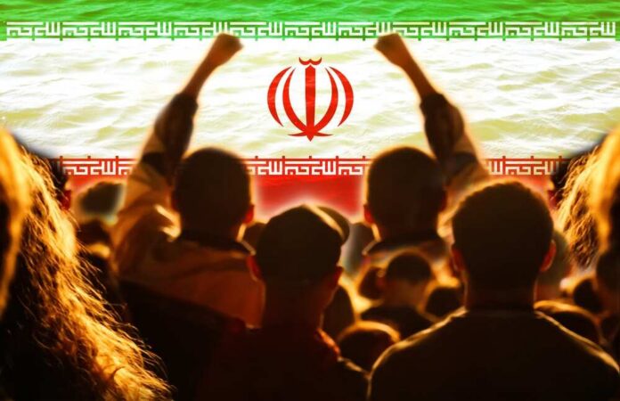 shutterstock_2724100193.jpg Crowd of people raising their fists in front of the Iranian flag