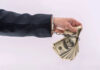 Handcuffed hand holding stack of hundred dollar bills