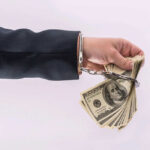Outrage: Developer’s $85M Fraud on Investors Handcuffed hand holding stack of hundred dollar bills