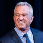 Smiling man wearing a suit against dark background.