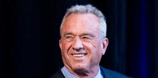 Smiling man wearing a suit against dark background.