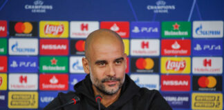 Football manager at a press conference with branding in the background