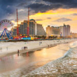 Beach scene at sunset with an amusement park and city buildings in the background