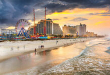 Beach scene at sunset with an amusement park and city buildings in the background