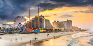 Beach scene at sunset with an amusement park and city buildings in the background