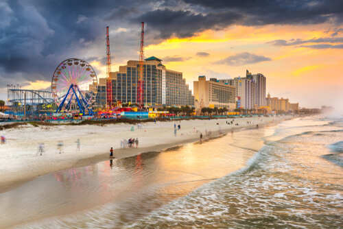 Beach scene at sunset with an amusement park and city buildings in the background