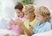 Three children sitting together, each using a smartphone