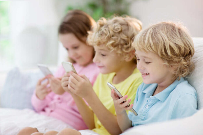 Three children sitting together, each using a smartphone