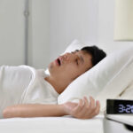 A man sleeping in bed with an alarm clock showing 3:20 AM