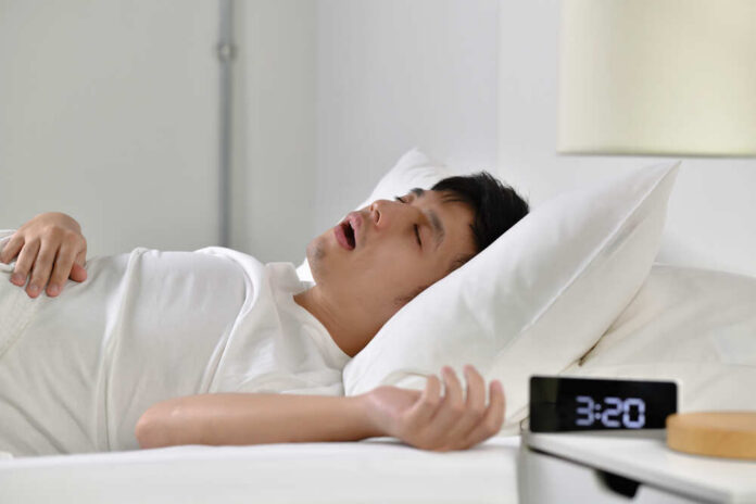A man sleeping in bed with an alarm clock showing 3:20 AM