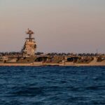 An aircraft carrier with the number 78 anchored in the ocean during sunset