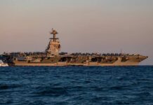 An aircraft carrier with the number 78 anchored in the ocean during sunset