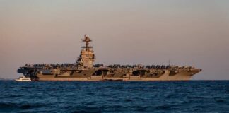 An aircraft carrier with the number 78 anchored in the ocean during sunset