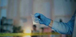 A gloved hand holding a plastic bag containing a suspicious substance at a crime scene