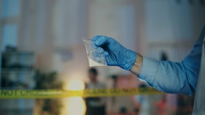 A gloved hand holding a plastic bag containing a suspicious substance at a crime scene