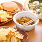 A variety of fast food items including fries, a burger, pizza, noodles, and a drink