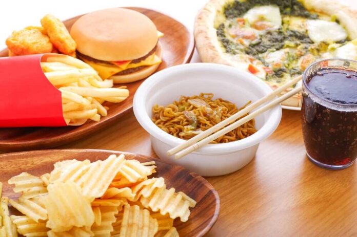 A variety of fast food items including fries, a burger, pizza, noodles, and a drink