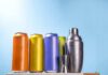 A lineup of colorful beverage cans next to a cocktail shaker and jigger
