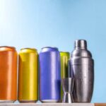 A lineup of colorful beverage cans next to a cocktail shaker and jigger