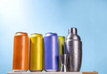 A lineup of colorful beverage cans next to a cocktail shaker and jigger