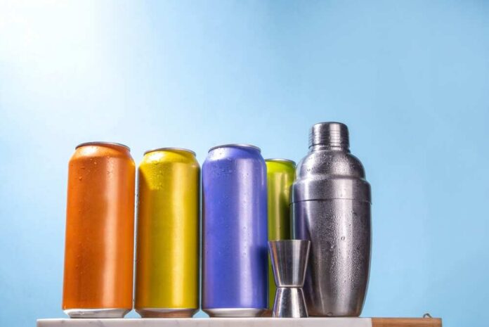 A lineup of colorful beverage cans next to a cocktail shaker and jigger