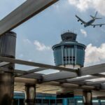 An airplane flying above an airport control tower under a cloudy sky