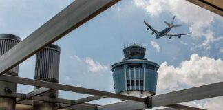 An airplane flying above an airport control tower under a cloudy sky