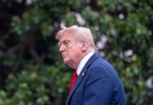 Profile view of a man in formal attire with a light-colored suit and red tie against a green background
