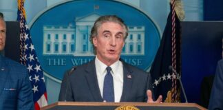 Government official speaking at a press conference in front of the White House seal