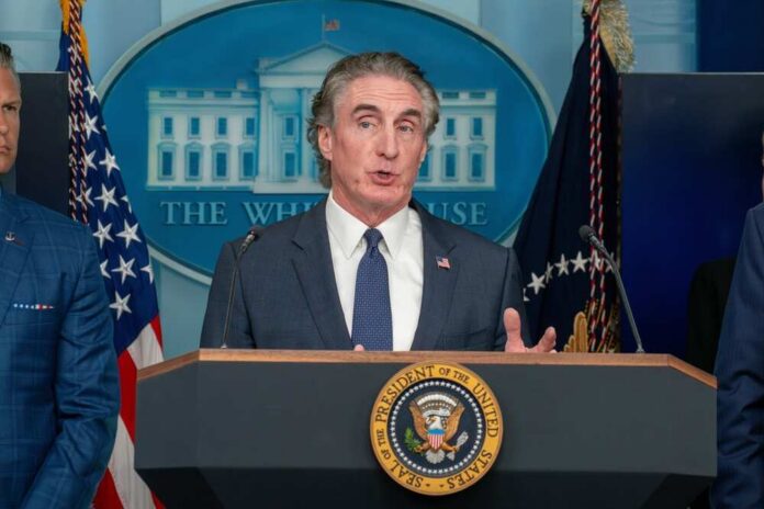 Government official speaking at a press conference in front of the White House seal
