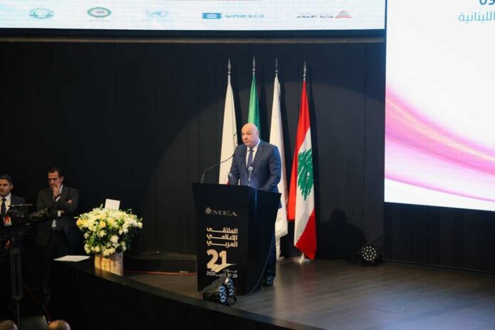 A speaker addressing an audience at a conference with Lebanese flags in the background