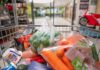 A shopping cart filled with various groceries including vegetables and canned goods