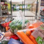 A shopping cart filled with various groceries including vegetables and canned goods