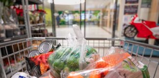 A shopping cart filled with various groceries including vegetables and canned goods
