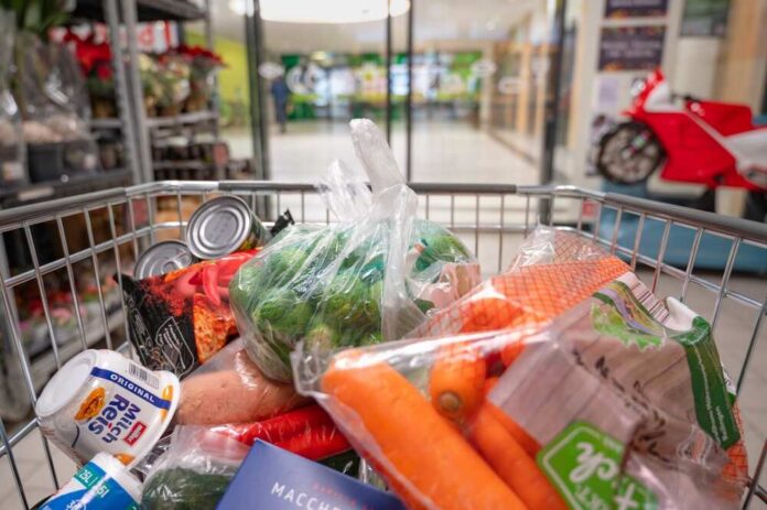 A shopping cart filled with various groceries including vegetables and canned goods