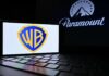 Warner Bros logo displayed on a smartphone with Paramount logo in the background
