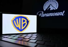 Warner Bros logo displayed on a smartphone with Paramount logo in the background