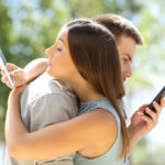 A couple standing back to back, each using their smartphones