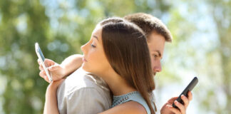 A couple standing back to back, each using their smartphones