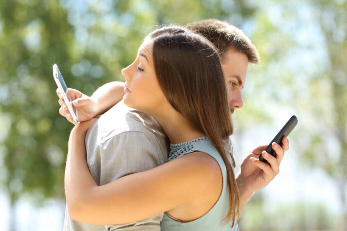 A couple standing back to back, each using their smartphones