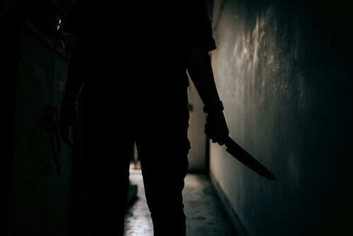 Silhouette of person holding knife in dark corridor