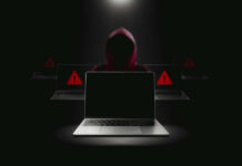 Hacker in hoodie behind laptops with warning signs