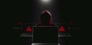 Hacker in hoodie behind laptops with warning signs