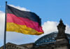 German flag waving against a blue sky near a historic building