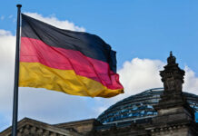 Germany’s Travel Trap: A Modern Freedom Threat? German flag waving against a blue sky near a historic building