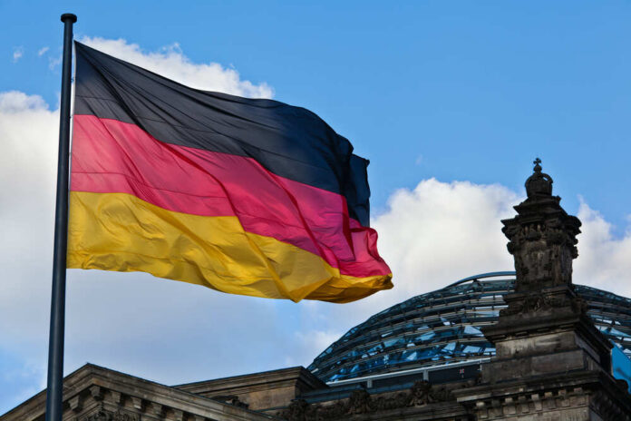 German flag waving against a blue sky near a historic building